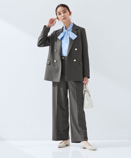 大きなリボンのシャツにグレーのセットアップを着た女性