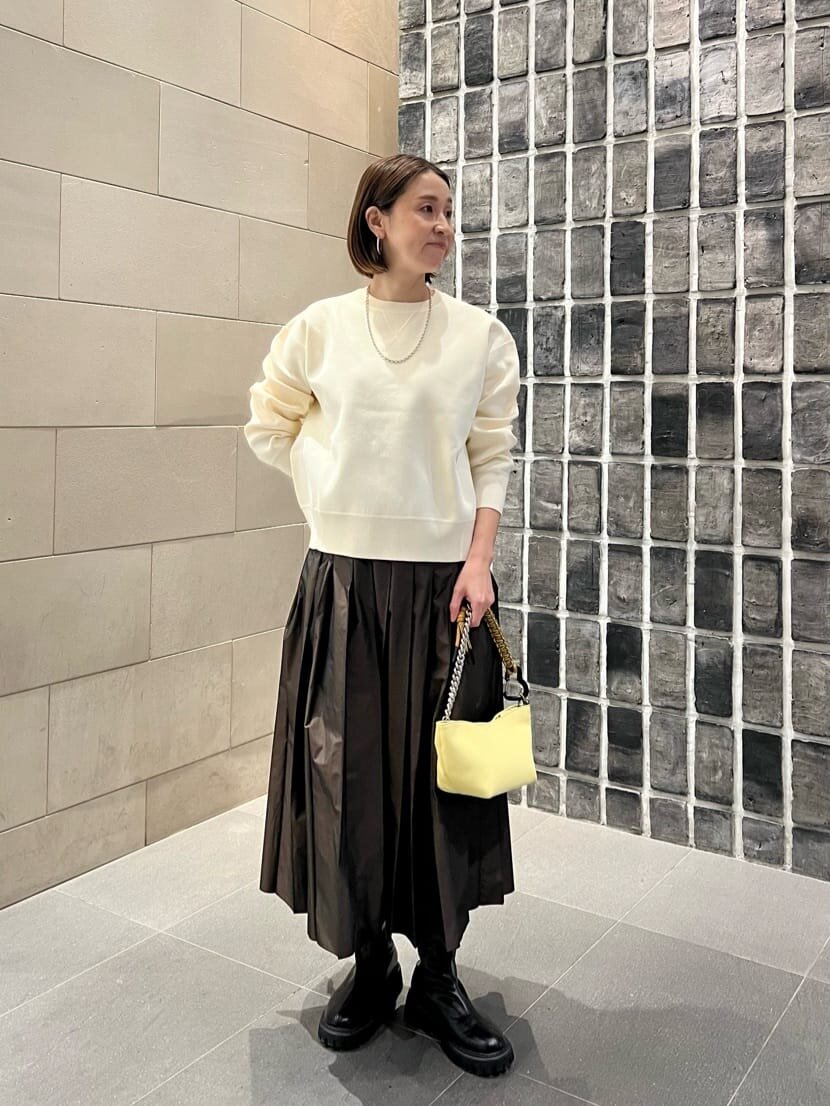 白いスウェットとブラウンのプリーツスカートを着た女性