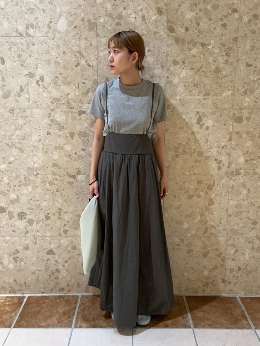 グレーのTシャツとカーキのキャミソールワンピースを着た女性