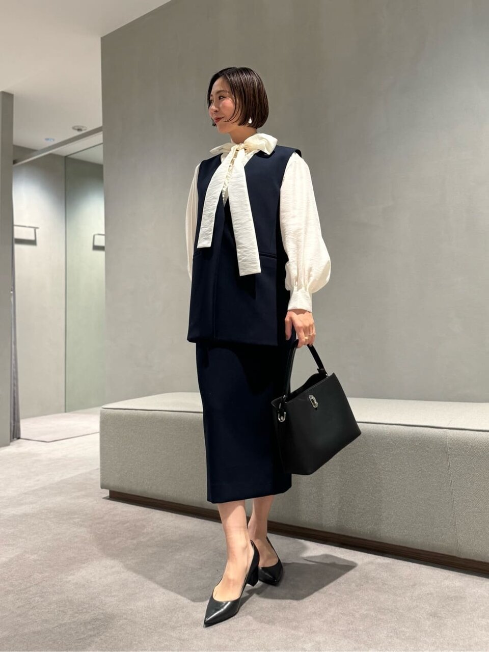ボウタイブラウスにベストとスカートをあわせた女性