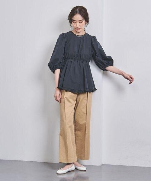ブラックのペプラムブラウスとベージュのワイドパンツを着用した女性