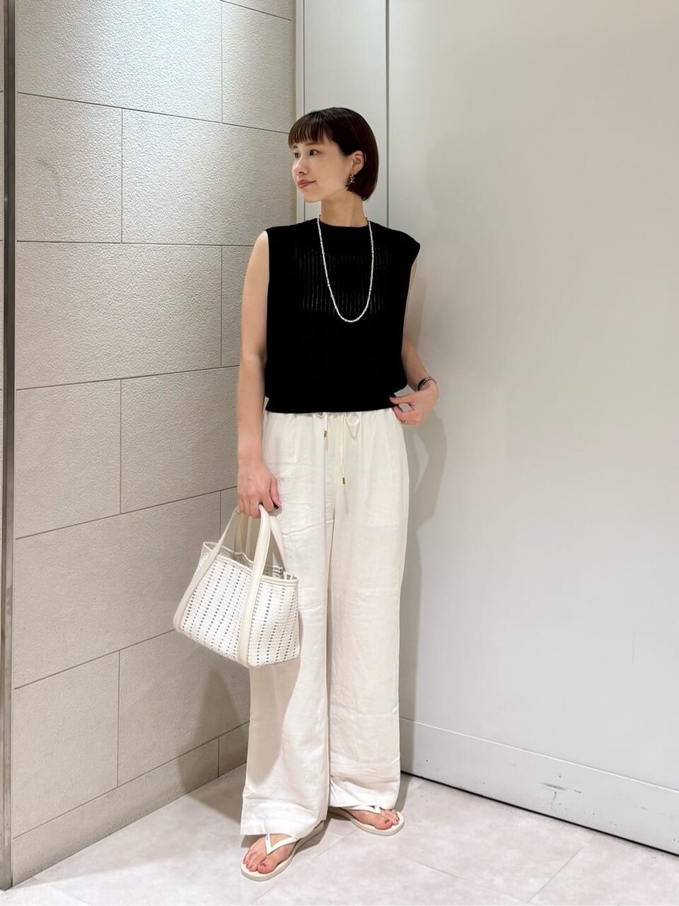 黒のノースリーブニットと白いパンツの女性