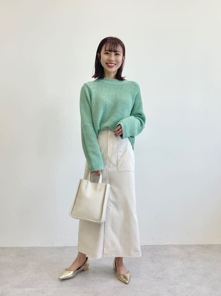 グリーンのニットと白いフレアスカートを履いた女性