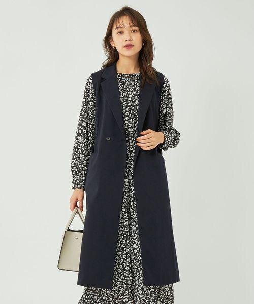 小花柄のワンピースと黒いロングジレを着た女性