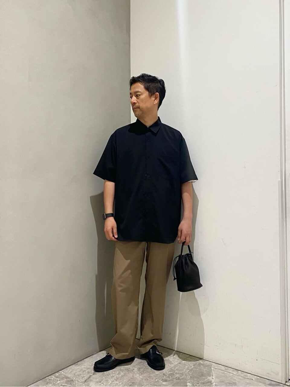 黒のシャツとベージュのパンツを着た男性