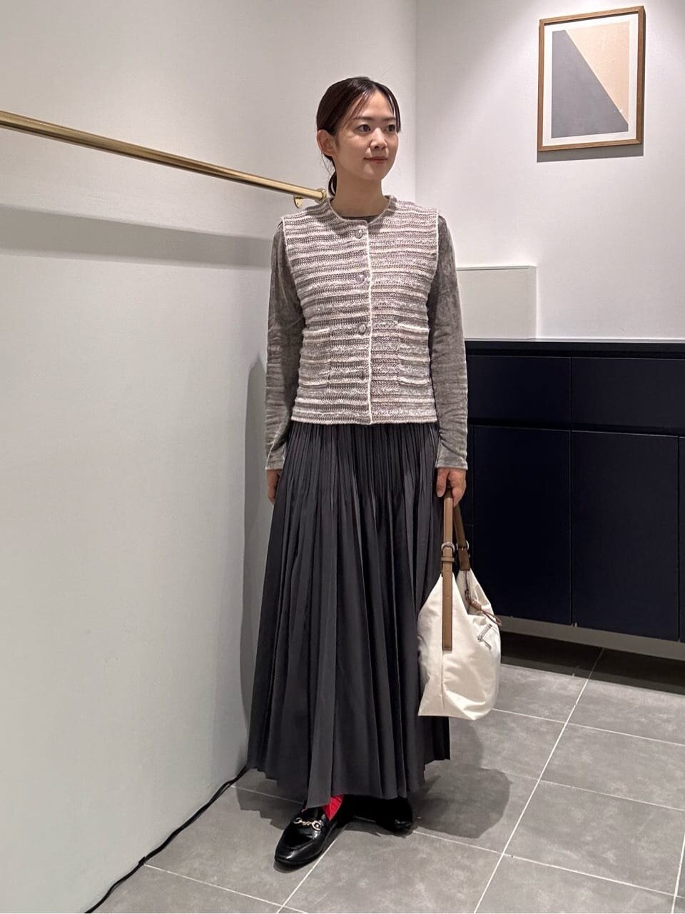 ツイード風ジレとプリーツスカートを着た女性