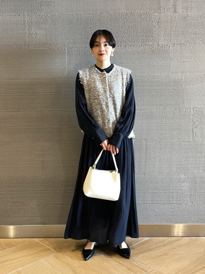 ネイビーのワンピースとグレーのベストを着た女性