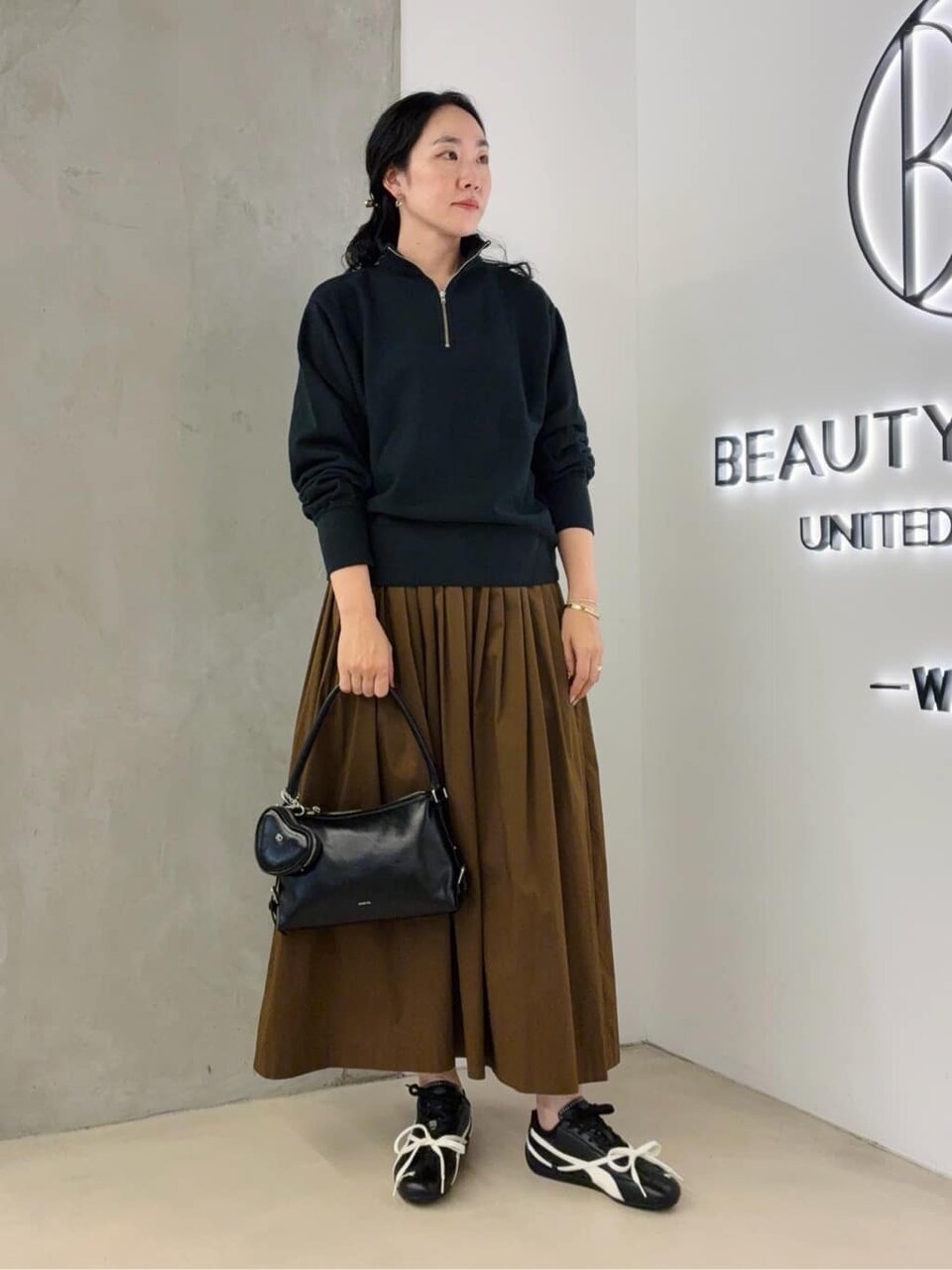 黒のスウェットと茶色いスカートを着た女性