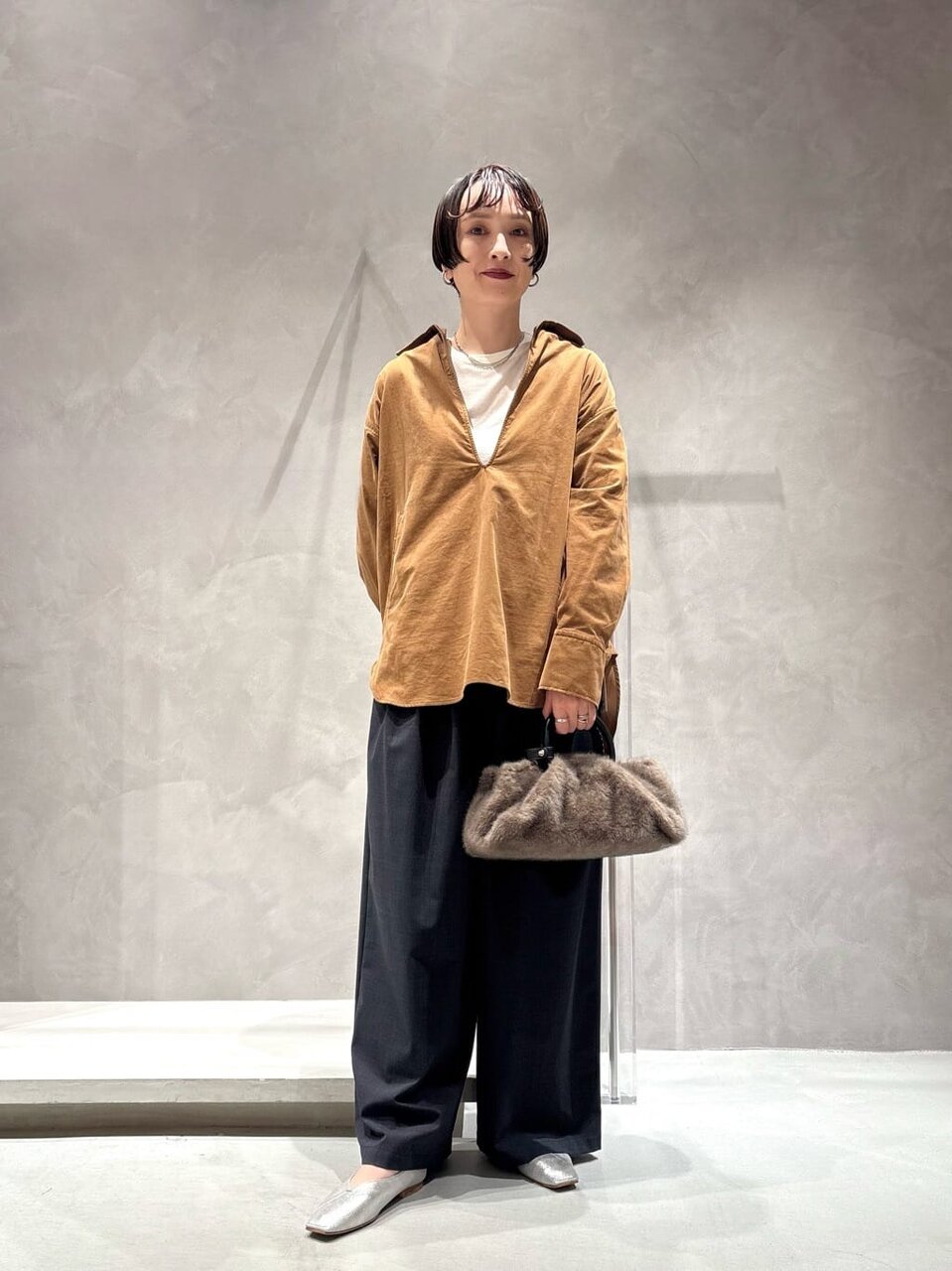 ブラウンのプルオーバーとグレーのパンツを着た女性