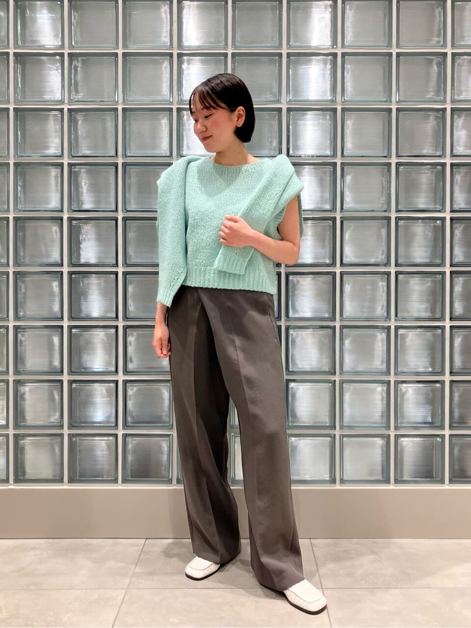 グリーンのニットとグレーのパンツを着た女性