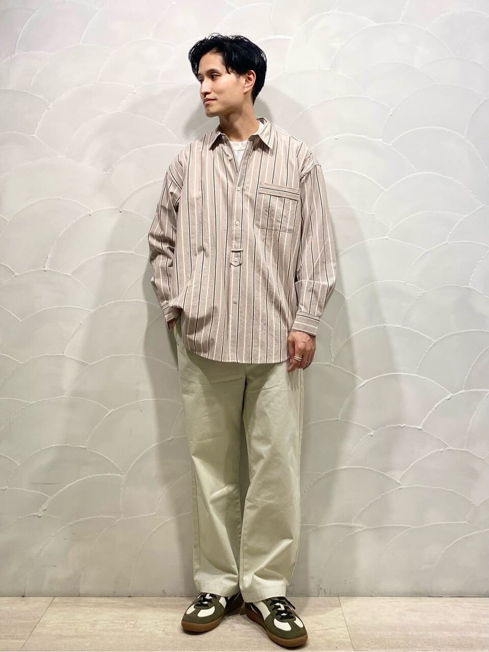 ストライプ柄シャツと淡い色のパンツを着た男性