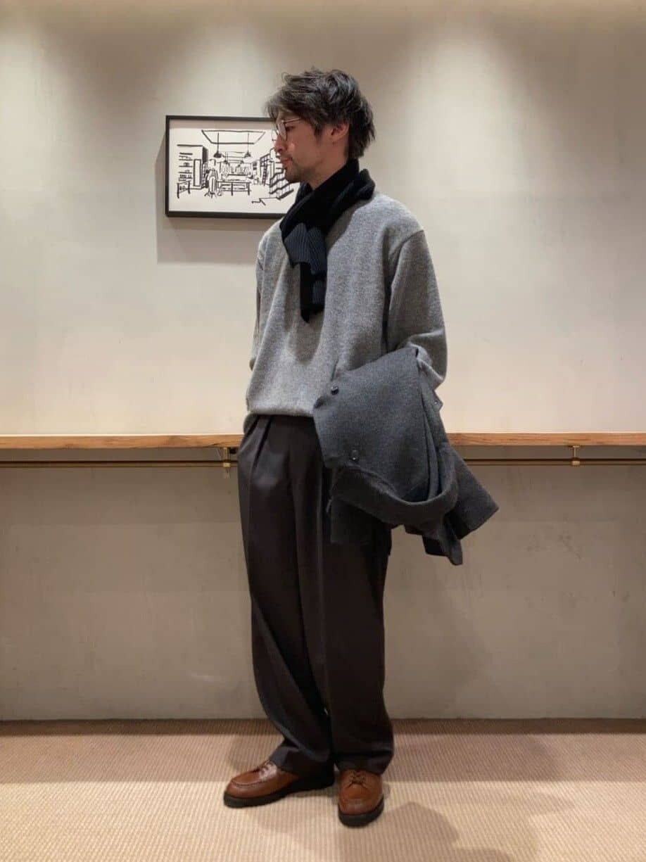 グレーのニットにスラックスをあわせた男性