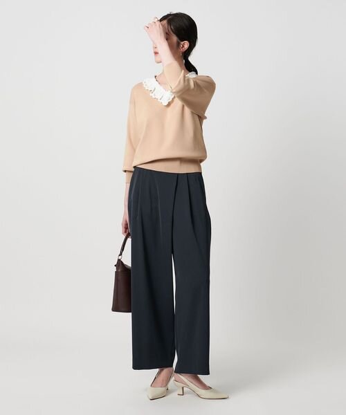 ベージュのブラウスと黒のチノパンコーデの女性