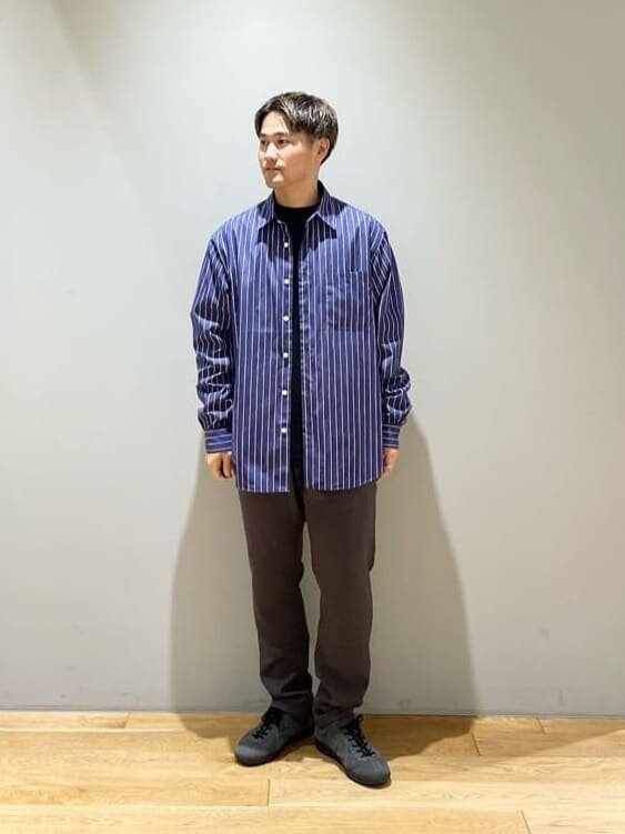 ネイビーのストライプ柄シャツとダークグレーのパンツを着た男性