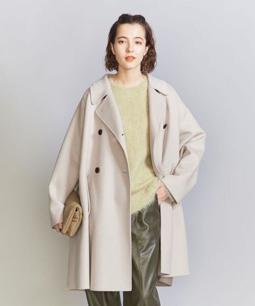 グリーンのニットにベージュのジャケットを羽織っている女性