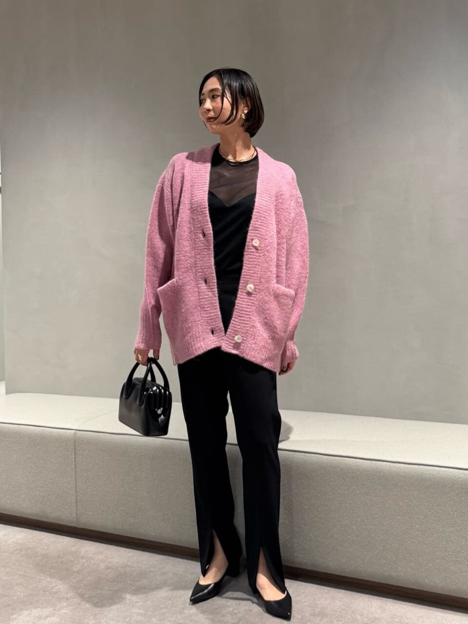 ピンクのカーディガンにパンツをあわせた女性