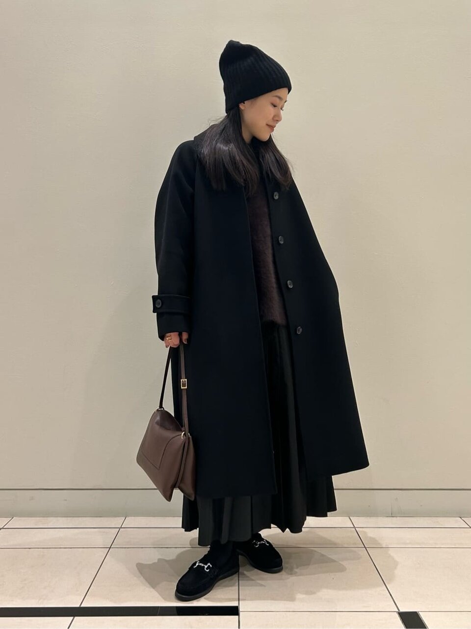 ステンカラーコートとプリーツスカートを着た女性