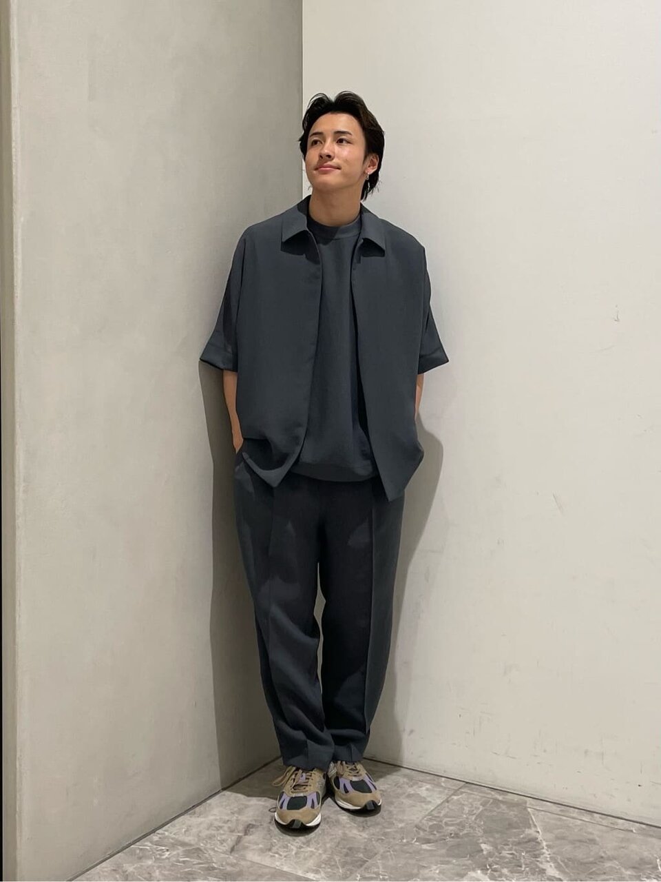 コーチジャケットとグレーのパンツを着た男性