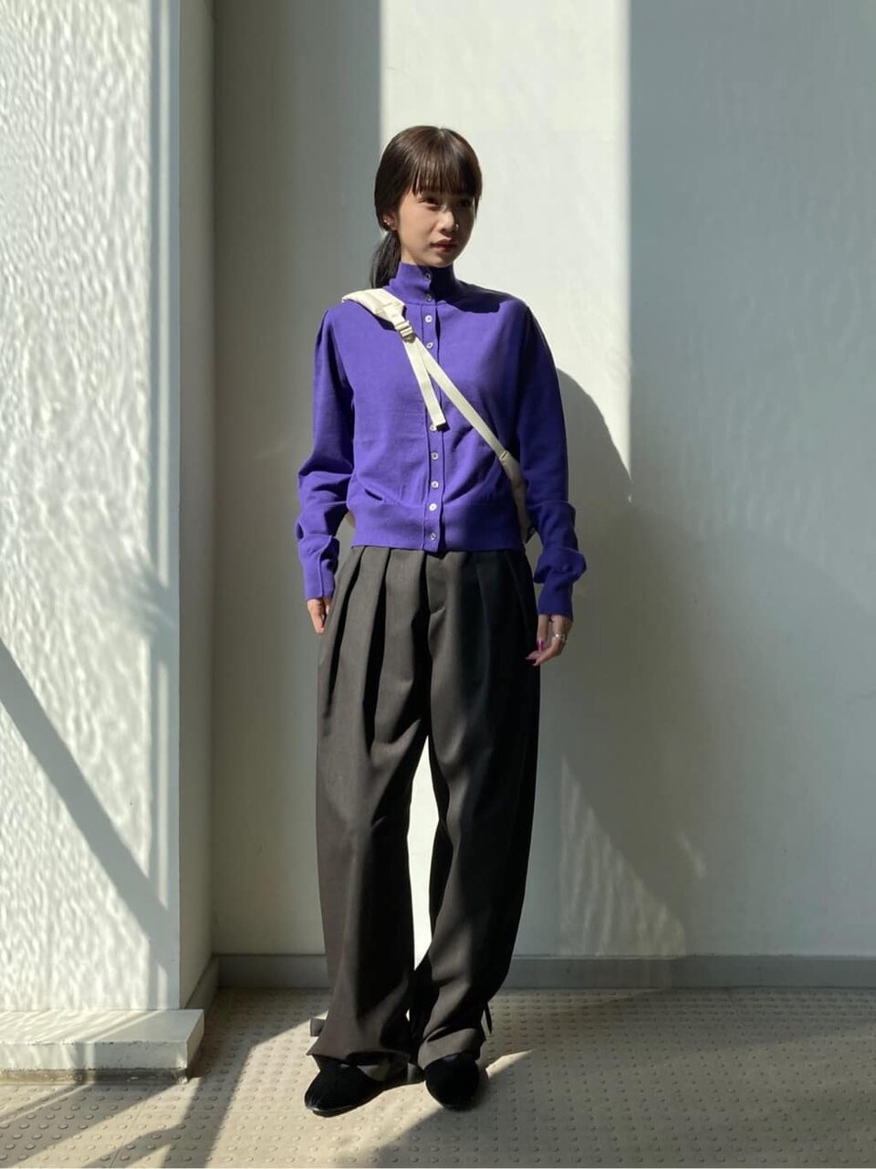 紫のカーディガンとブラウンのパンツを着た女性
