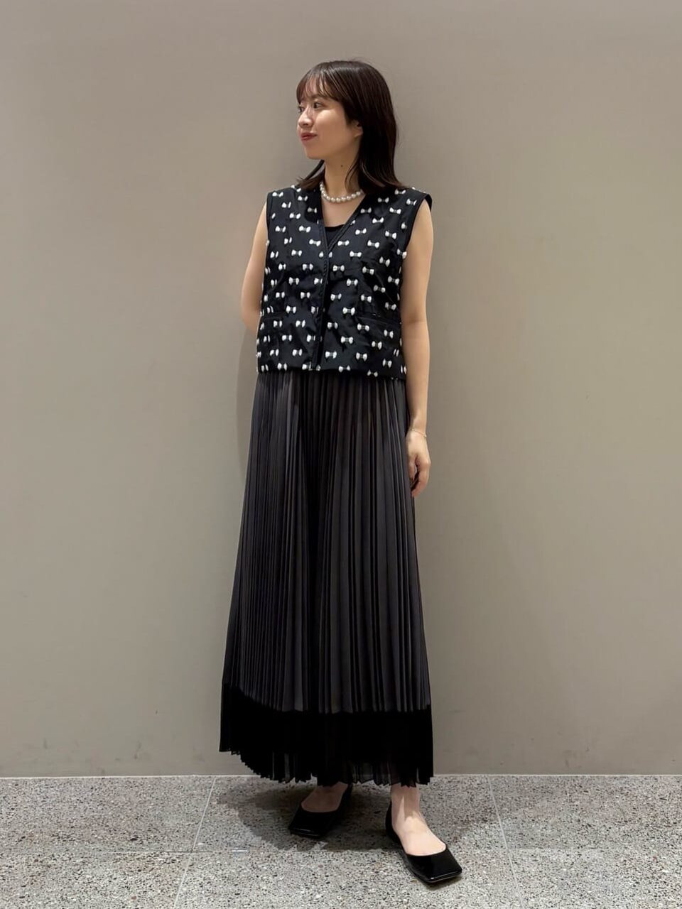 ノーカラーベストとプリーツスカートを着た女性