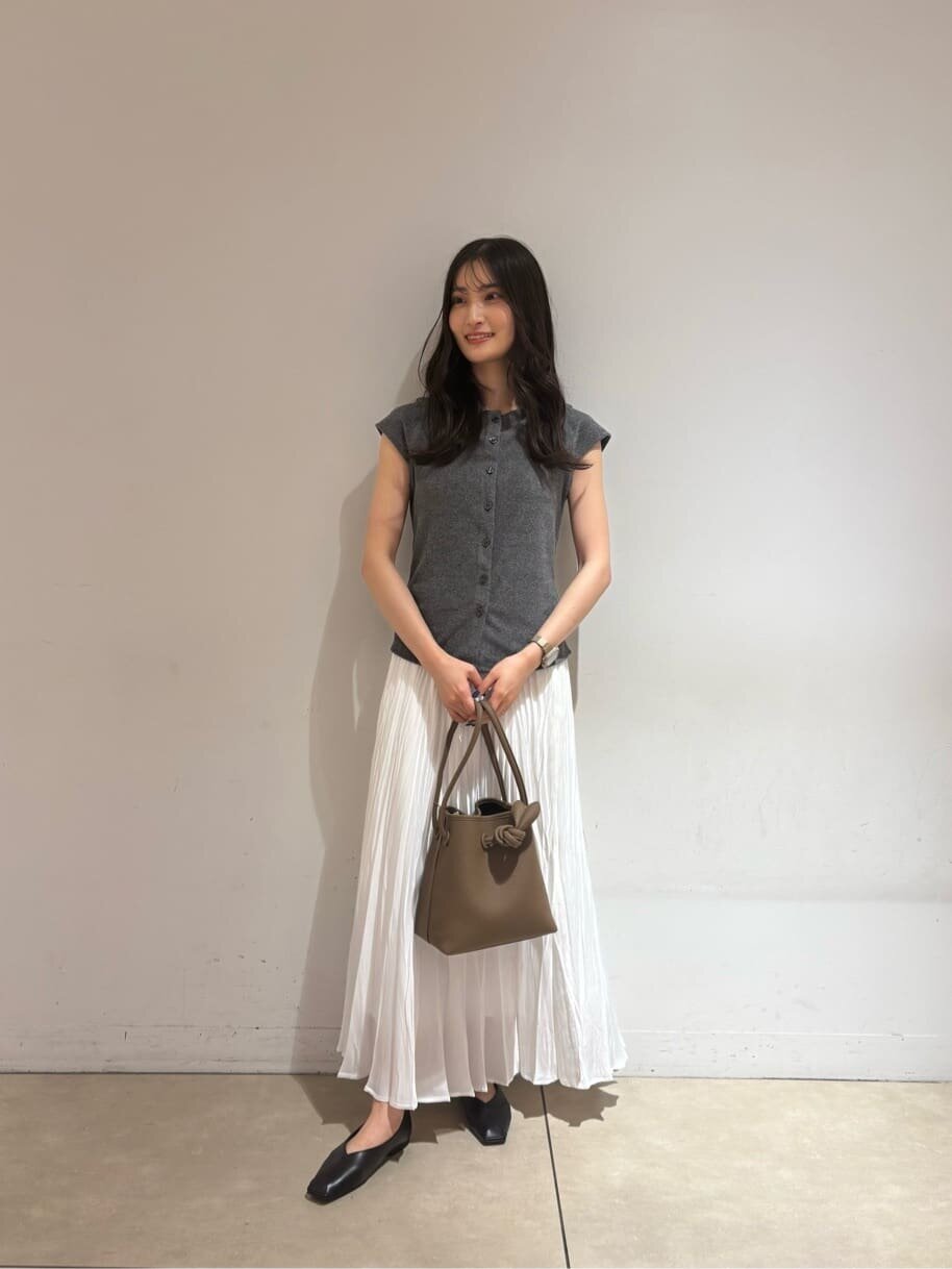 グレーのトップスと白のプリーツスカートを着た女性