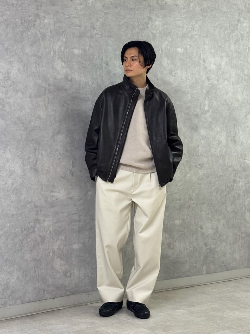 ダークブラウンのレザージャケットにナチュラルカラーのパンツをあわせた男性