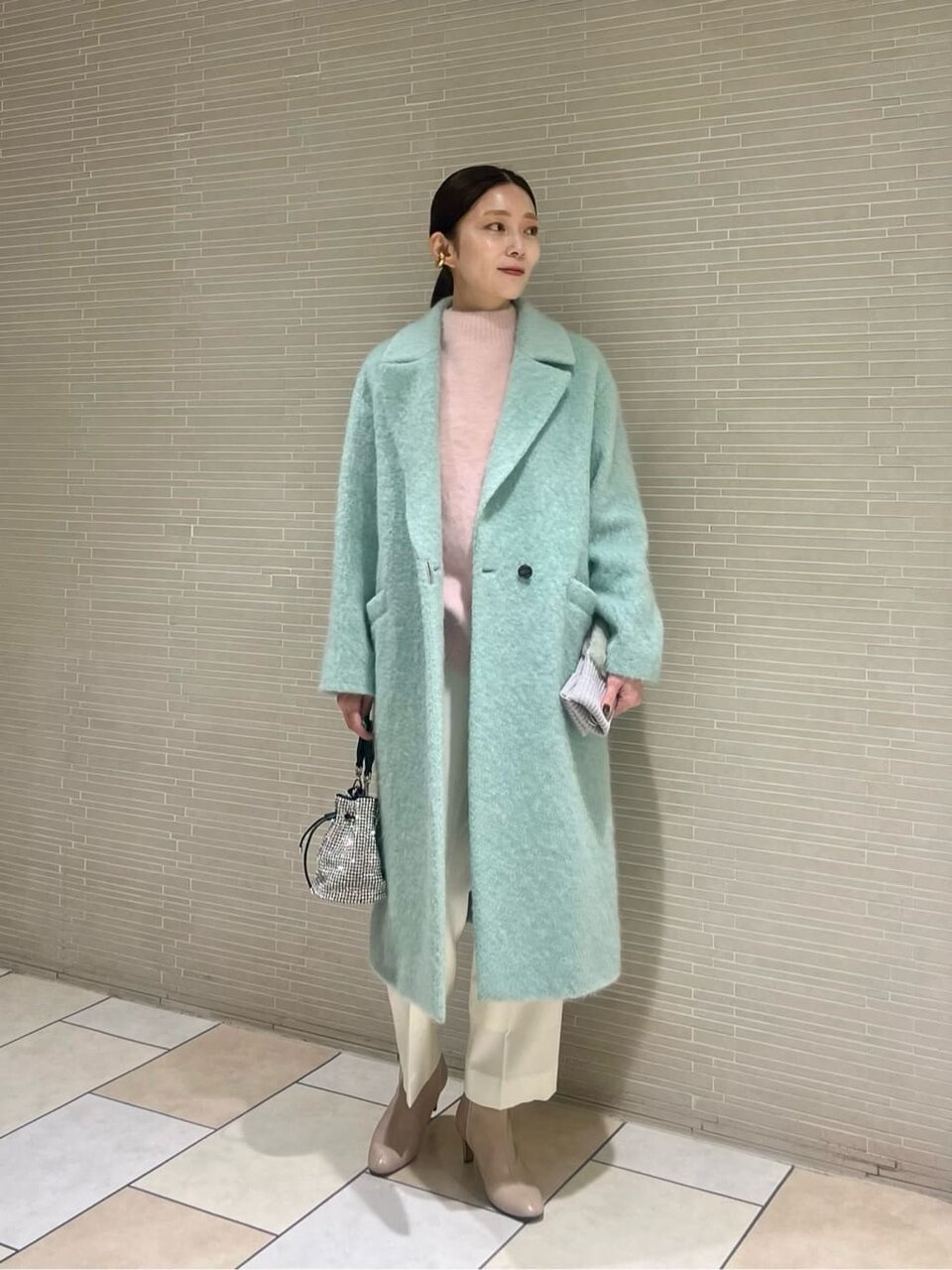 ライムカラーのコートに白いパンツを着た女性