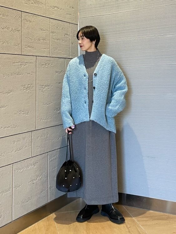 グレーのワンピースにブルーのニットカーディガンを着た女性