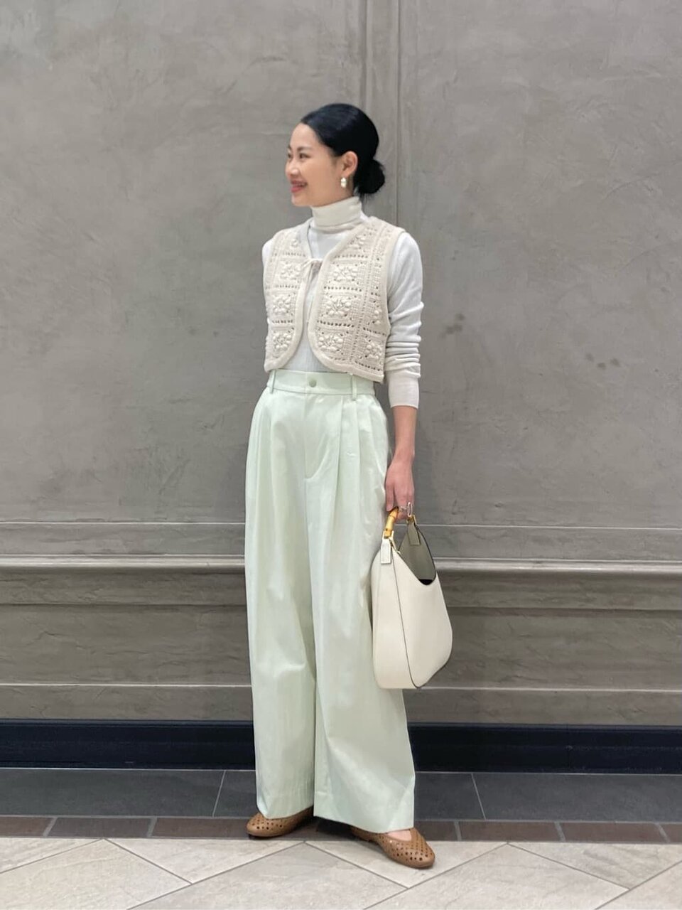 白いニットベストとグリーンのパンツを着た女性