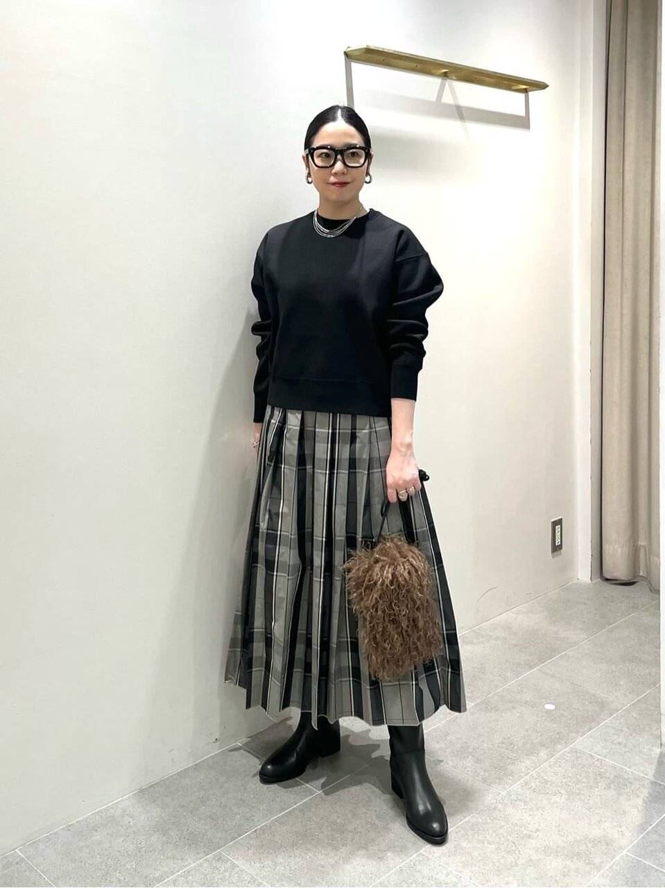 黒のトップスにチェックのプリーツスカートを着た女性