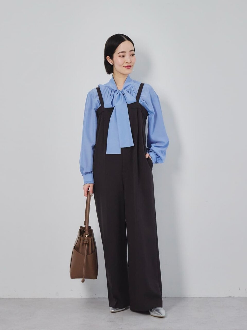 ブルーのボウタイブラウスとサロペットを着た女性