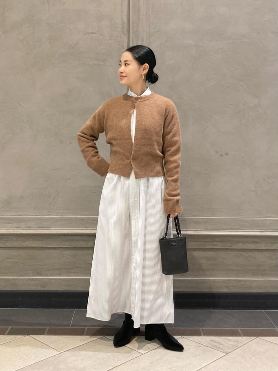 白いワンピースにベージュカーディガンを着た女性