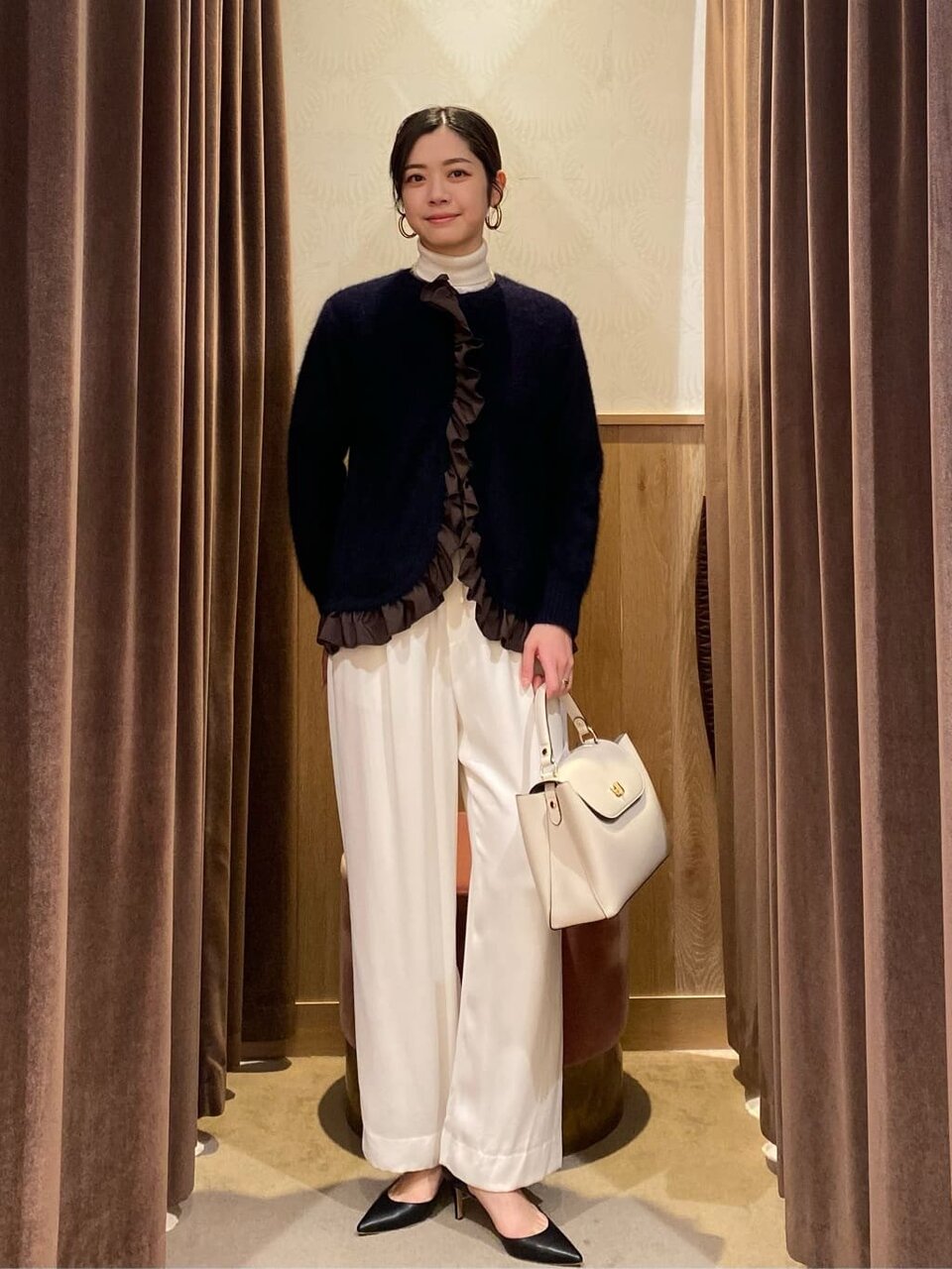 フリルカーディガンと白いパンツを着た女性