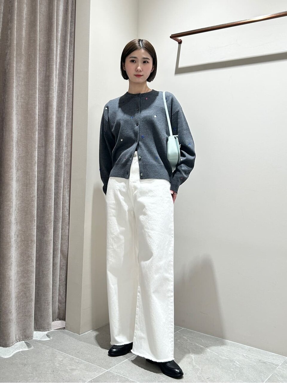 グレーのカーディガンと白いパンツを着た女性