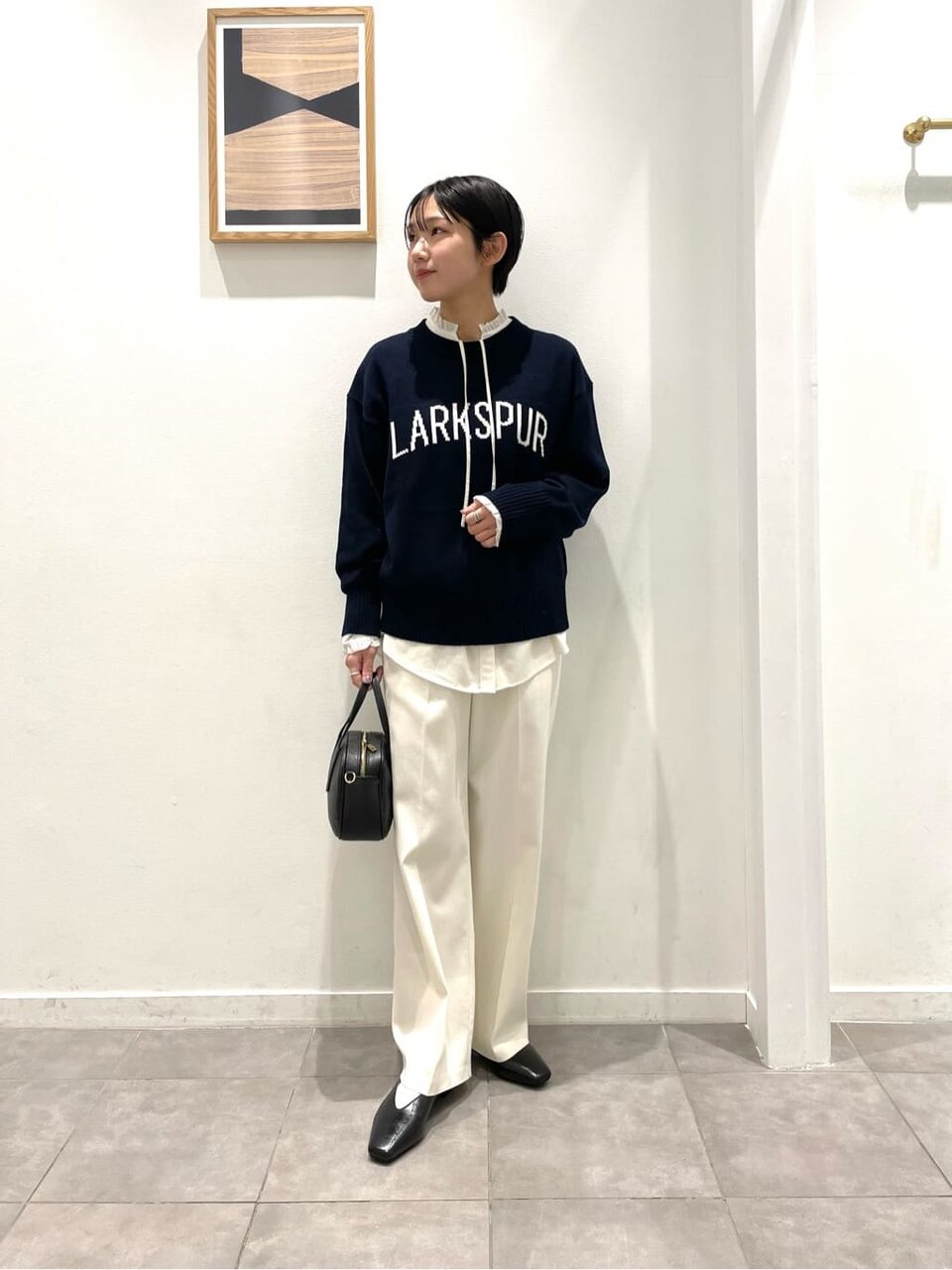 ロゴニットと白いパンツを着た女性