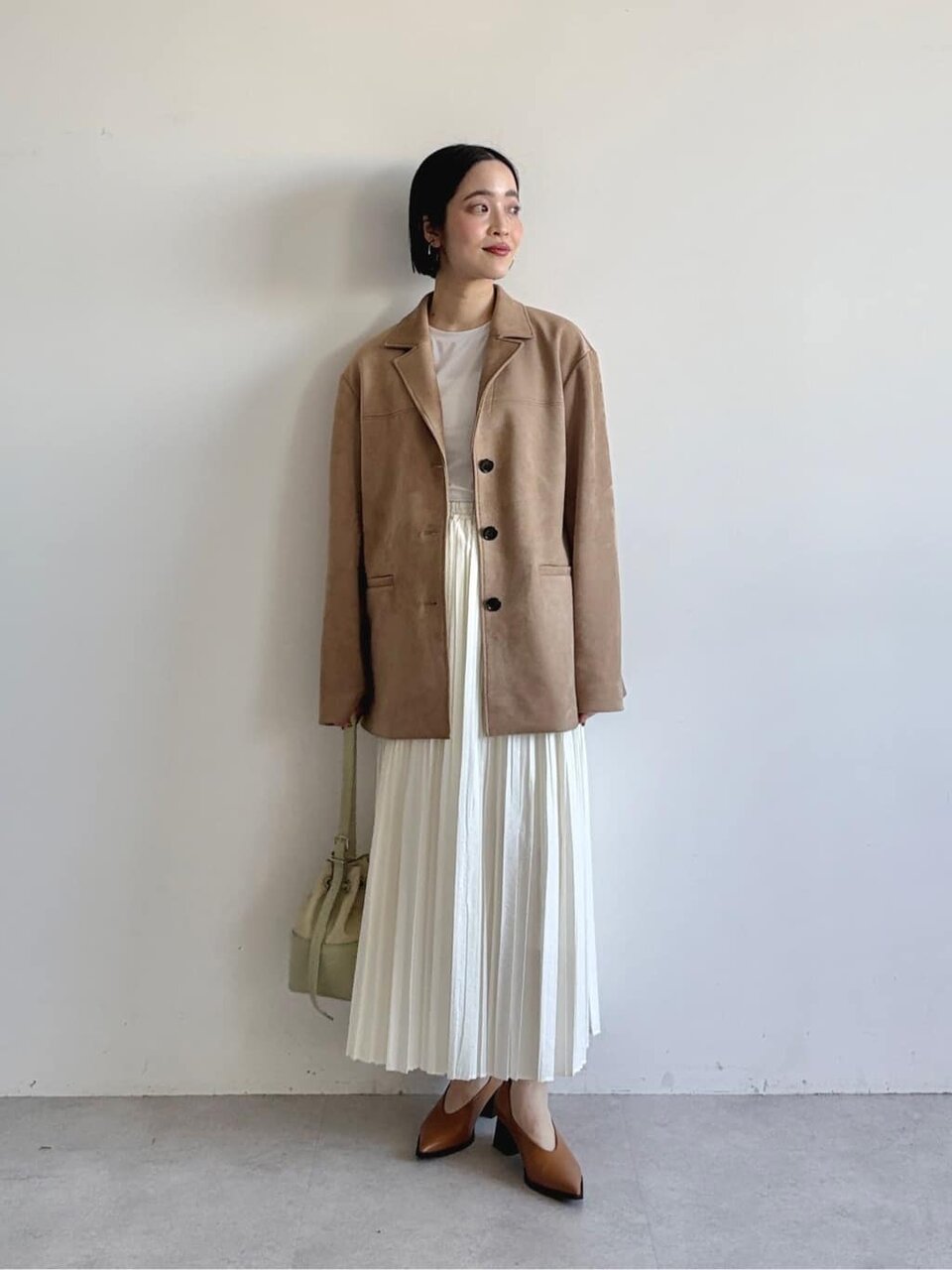 ベージュのジャケットと白のプリーツスカートを着た女性