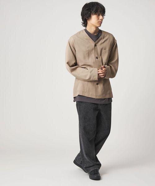 ベージュジャケットにデニムパンツをあわせた男性