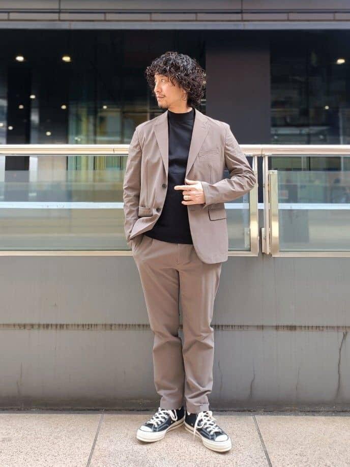ベージュジャケットに黒のインナーをあわせた男性