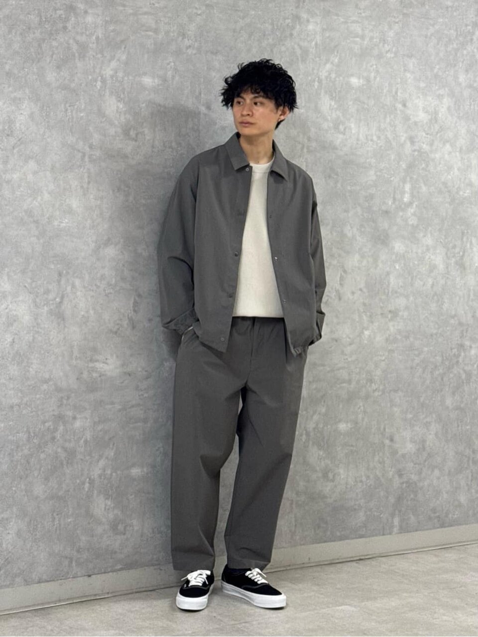 コーチジャケットとグレーのパンツを着た男性