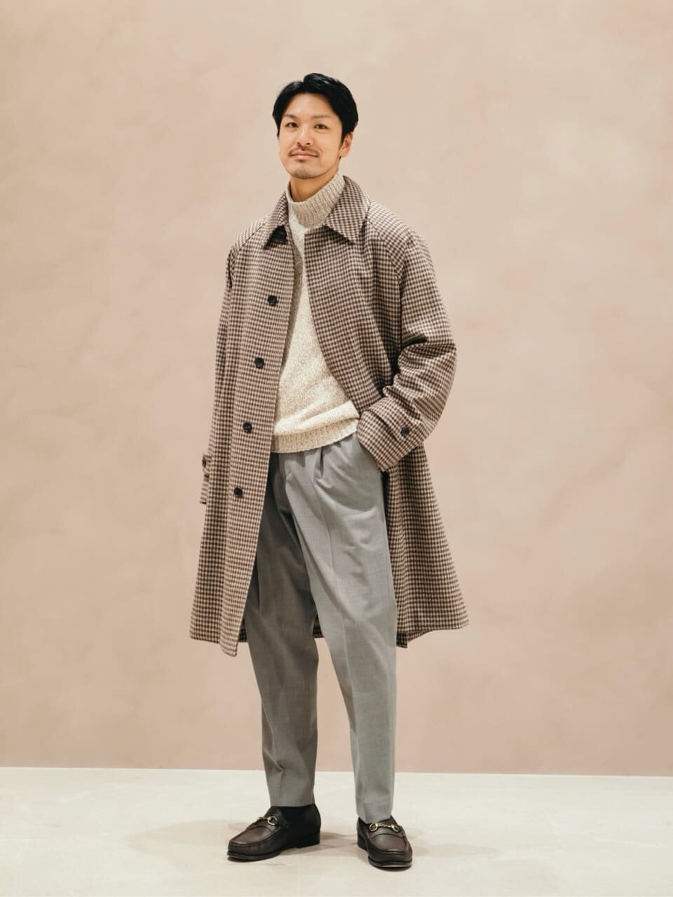 ステンカラーコートとグレーのパンツを着た男性