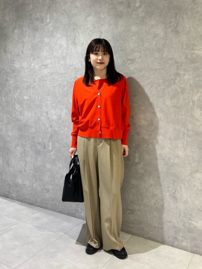 赤のカーディガンとベージュのパンツを着た女性