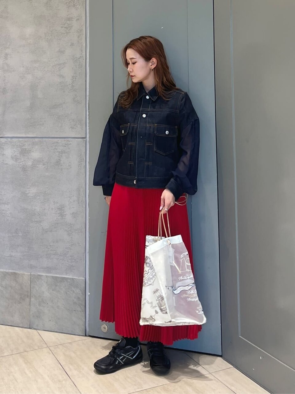 デニムジャケットと赤いプリーツスカートを着た女性