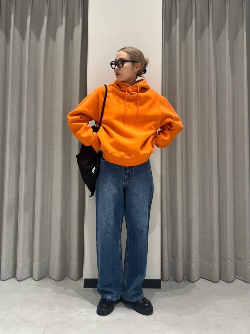 オレンジのパーカーとハイウエストデニムを着た女性