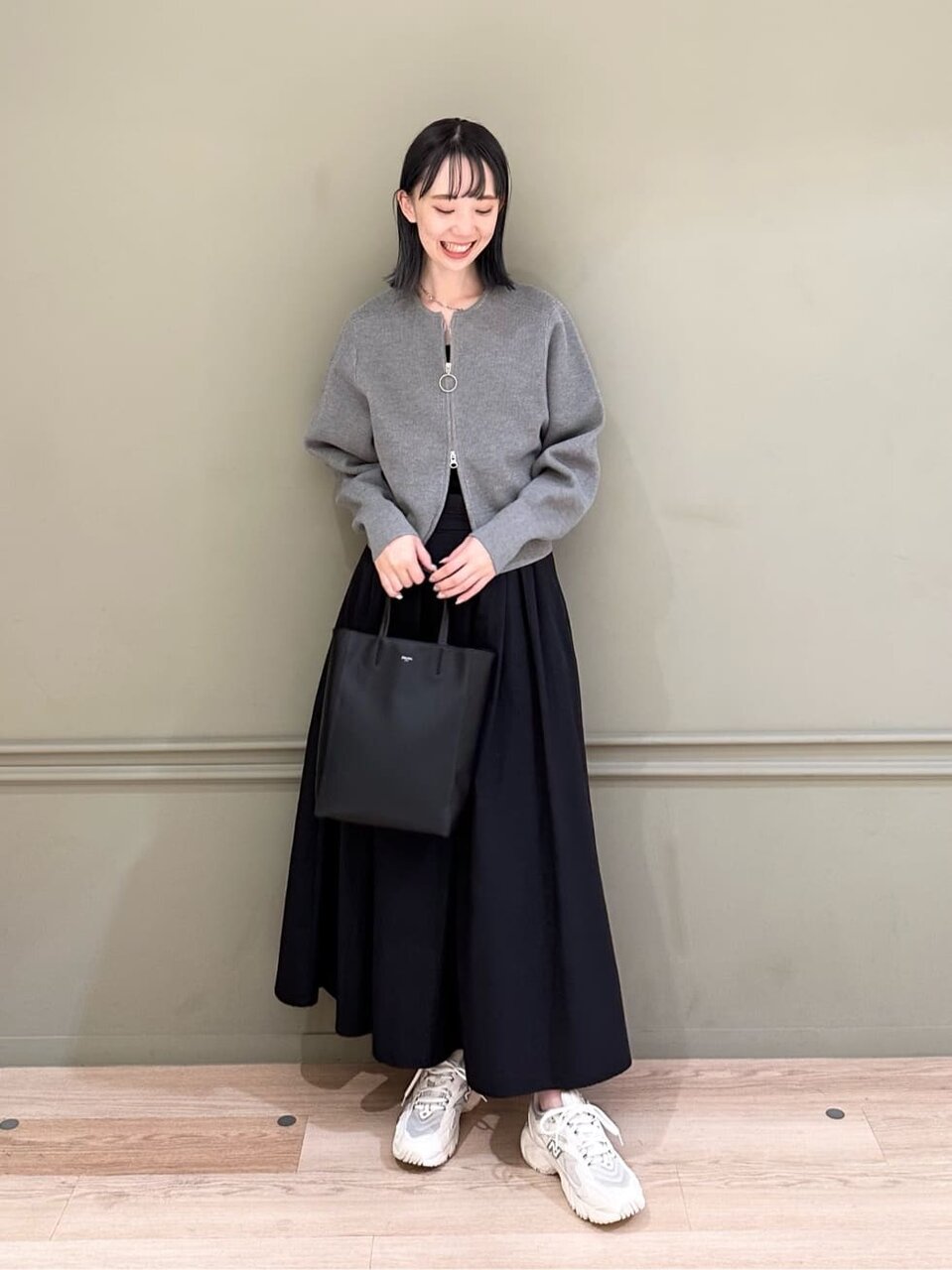 グレーのカーディガンと黒のスカートをはいた女性