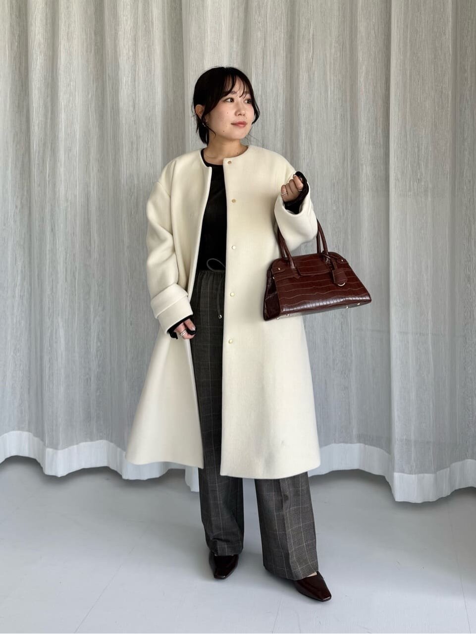 白のノーカラーコートとスラックスを着た女性