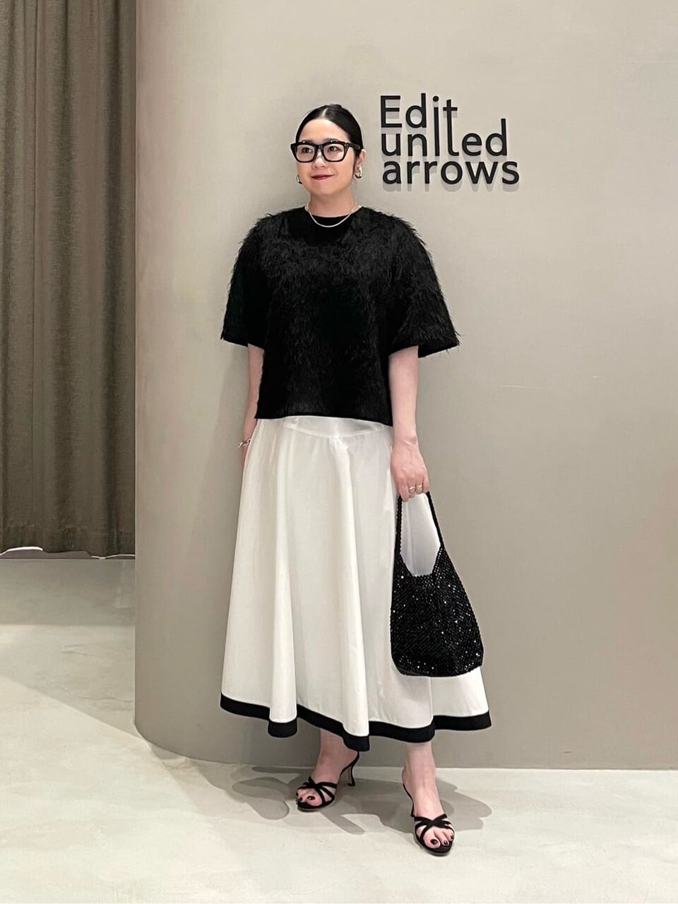 黒のフリンジTシャツと白のスカートを着た女性