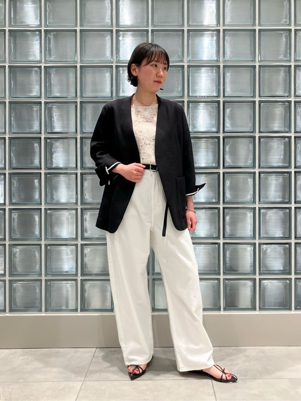 黒のノーカラージャケットと白のデニムパンツを着た女性