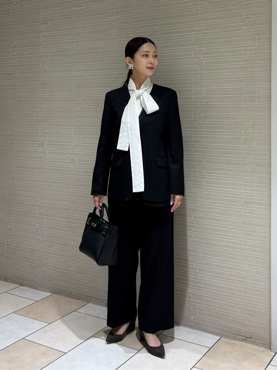 黒のノーカラージャケットとボウタイブラウスを着た女性