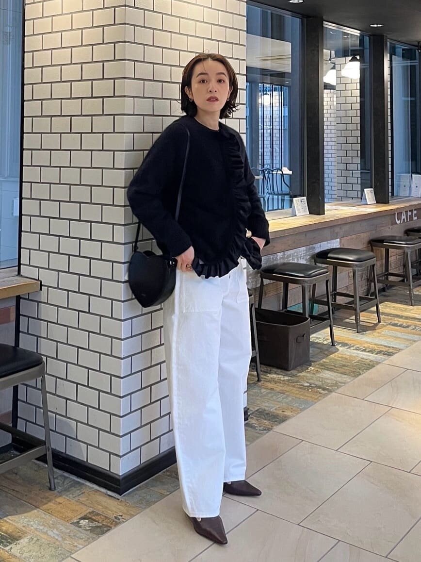 黒フリルニットと白のワイドパンツを着た女性