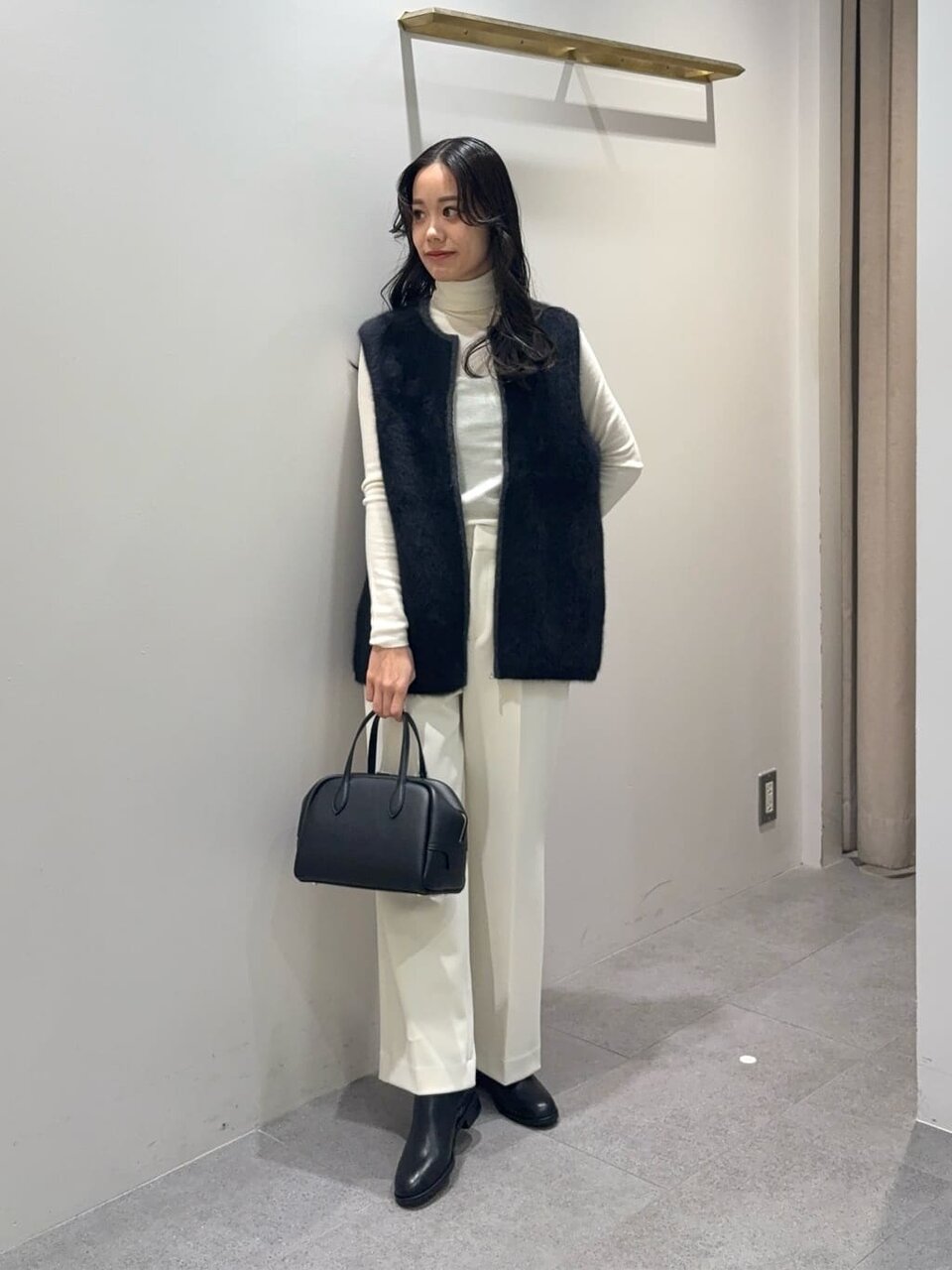 黒のニットジレと白のワイドパンツを着た女性